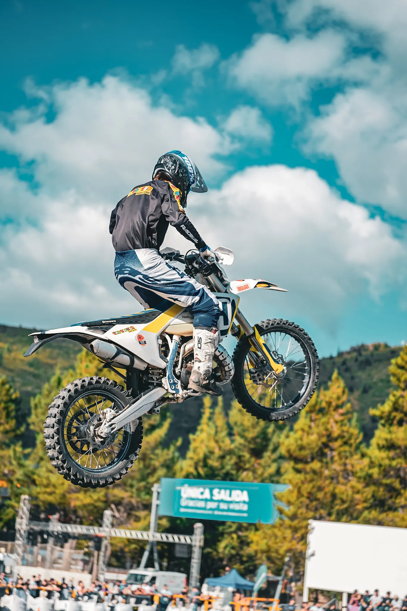 Moto de freestyle volando por el aire con el cerro y el bosque de fondo en Bariloche