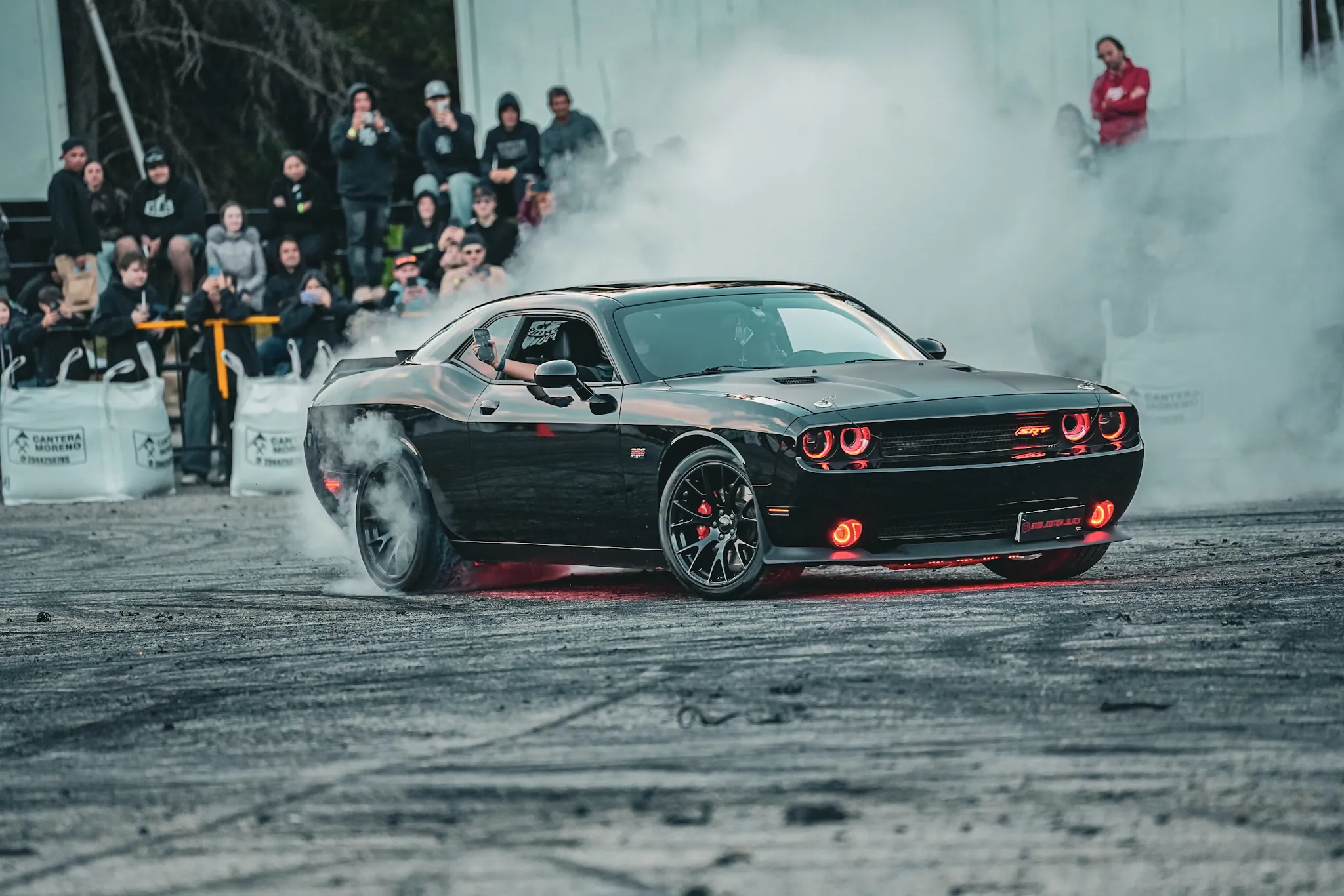 Dodge Challenger negro haciendo burnout con humo y público en Bariloche